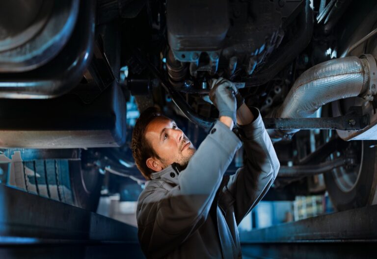 An automotive repair technician inspecting the underside of a vehicle in Central Minnesota
